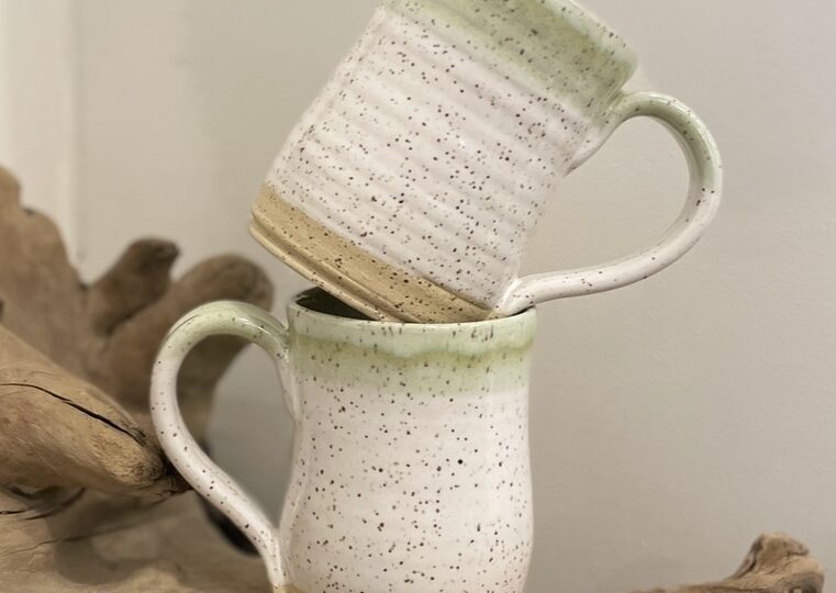 two speckled pottery mugs with green and beige colour detail stacked on top wood