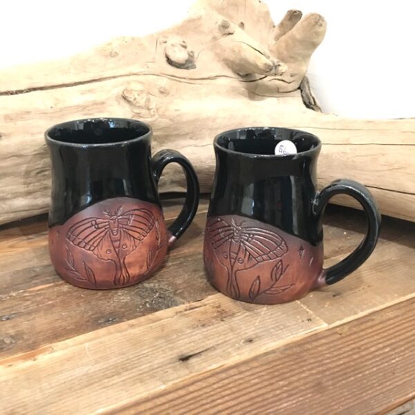 two Black and clay Pottery Mugs with moth and leaves engraved on wood table