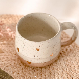 white speckled Pottery Mug with light pink bottom and tiny gold hearts on wicker placemat